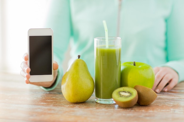 alimentación saludable, tecnología, dieta y concepto de personas - cierre de manos de mujer con smartphone, frutas y jugo fresco sentado en la mesa