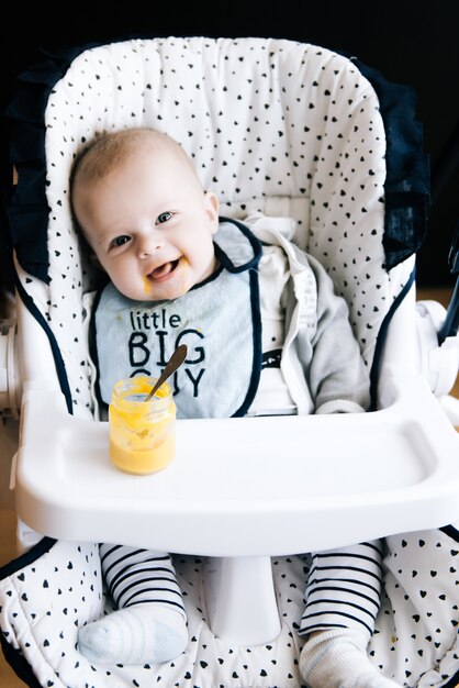 Alimentando. Criança adorável bebê comendo com uma colher na cadeira alta. bebê