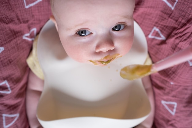 Alimentando a un pequeño bebé caucásico en un babero con una cuchara por primera vez