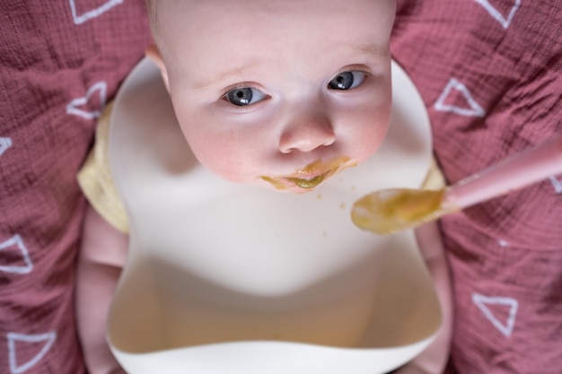 Alimentando um bebê caucasiano em um babador com uma colher pela primeira vez