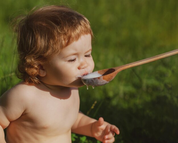 Alimentar al bebé con una cuchara grande al aire libre sobre hierba verde