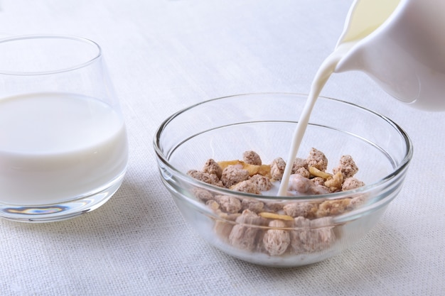 Alimento saudável com cereal dos flocos de milho em uma bacia, em uma maçã, em uma banana e em um vidro com leite.