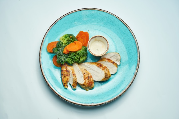 Alimento saudável, dietético - filé de frango assado com cenouras e brócolis cozidos em uma placa de cerâmica azul isolada luz - superfície cinza.