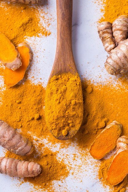 Alimentos y bebidas, nutrición dietética, concepto de atención médica. Raíz y polvo de cúrcuma naranja orgánica cruda, curcuma longa sobre una mesa de cocción. Especias orientales indias bajas en colesterol