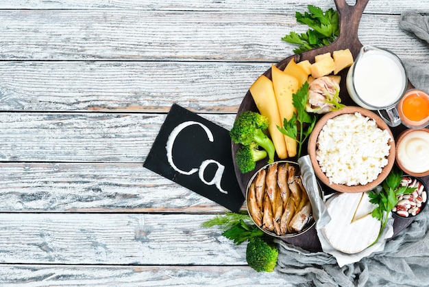 Foto alimentos con calcio una variedad de alimentos ricos en calcio queso leche parmesano crema agria pescado almendras perejil ajo brócoli sobre un fondo blanco de madera vista superior espacio de copia libre