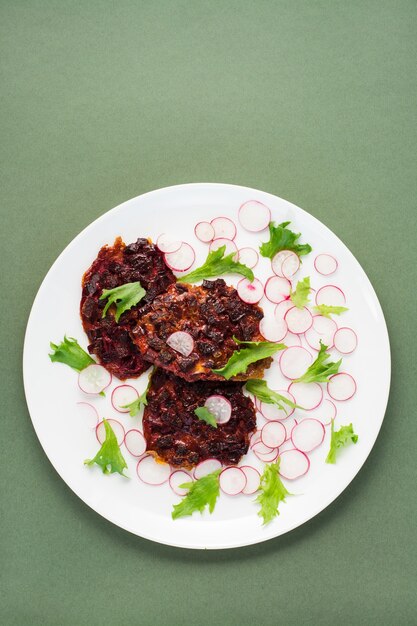 Alimentos dietéticos vegetales. Filete de remolacha, ensalada de rábano y friso de hojas en un plato sobre una mesa verde. Vista vertical, espacio de copia