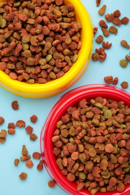 Alimentos húmedos y secos para mascotas en tazones de alimentación sobre fondo azul Foto vertical
