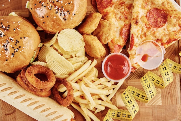 Foto alimentos no saludables y chatarra diferentes tipos de comida rápida y bocadillos en la mesa con cinta métrica