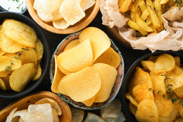 Alimentos o refrigerios poco saludables Todos los refrigerios clásicos de papa con palomitas de maíz y aros de cebolla y pretzels salados en platos de tazón sobre fondo de madera vieja Alimentos poco saludables para los dientes de la piel del corazón de la figura