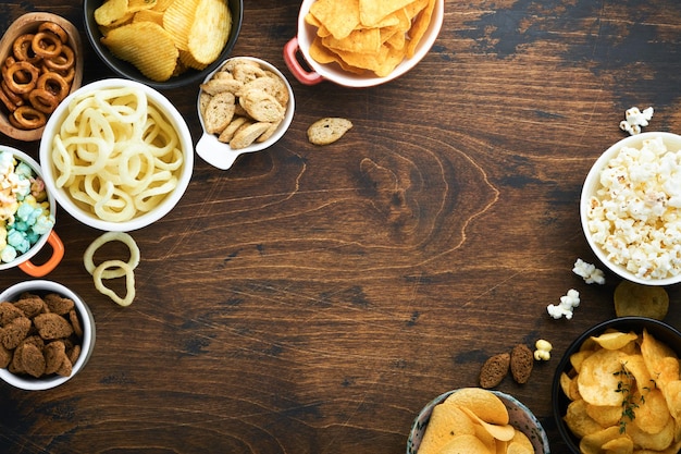 Alimentos o refrigerios poco saludables Todos los refrigerios clásicos de papa con palomitas de maíz y aros de cebolla y pretzels salados en platos de tazón sobre fondo de madera vieja Alimentos poco saludables para los dientes de la piel del corazón de la figura