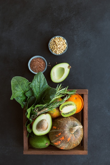 Alimentos orgánicos de agricultores saludables en caja de madera: frutas, verduras, semillas, superalimento, verdura de hoja sobre fondo negro. Concepto de selección de alimentación limpia