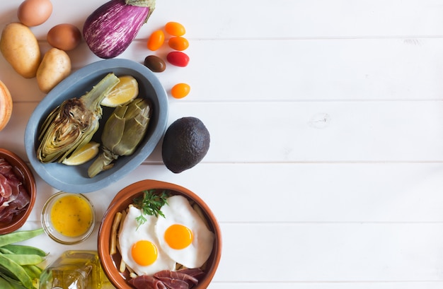 Foto alimentos orgânicos na mesa branca. alcachofras e limões no prato. ovos fritos e legumes. este produto as pessoas costumam comer no almoço saudável