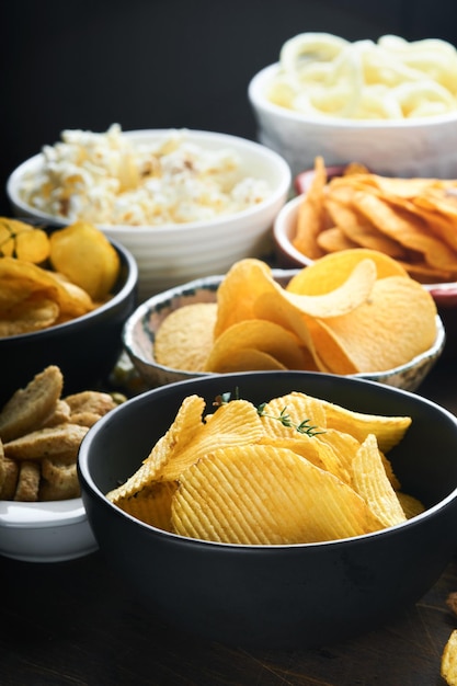 Alimentos ou lanches não saudáveis Todos os lanches clássicos de batata com pipoca de amendoim e anéis de cebola e pretzels salgados em pratos de tigela sobre fundo de madeira velho Alimentos não saudáveis para dentes de pele de coração de figura