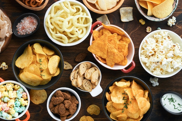 Alimentos ou lanches não saudáveis Todos os lanches clássicos de batata com pipoca de amendoim e anéis de cebola e pretzels salgados em pratos de tigela sobre fundo de madeira velho Alimentos não saudáveis para dentes de pele de coração de figura