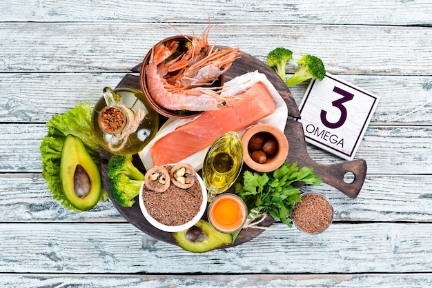 Alimentos que contêm ômega 3 Vitamina Alimentos saudáveis abacates peixes camarão brócolis linho nozes ovos salsa Vista superior Espaço livre para o seu texto Em um fundo branco de madeira