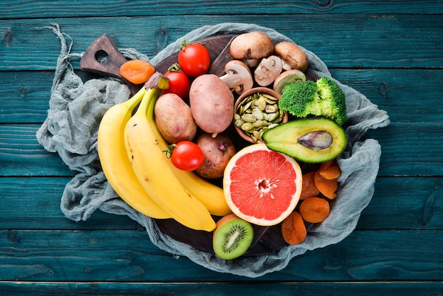 Alimentos que contienen potasio natural. K: papas, champiñones, plátano, tomates, nueces, frijoles, brócoli, aguacates. Vista superior. Sobre un fondo de madera azul.