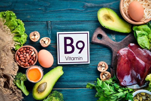 Alimentos que contienen vitamina B9 natural: hígado, aguacate, brócoli, espinacas, perejil, frijoles, nueces, sobre un fondo azul. Vista superior.