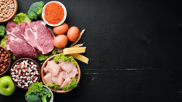 Alimentos ricos en proteínas. Nutrición saludable o concepto de dieta. Carne, filete de pollo, brócoli, frijoles, queso, huevos, trigo. Sobre un fondo negro.