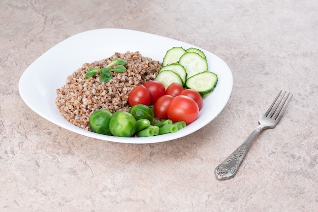 Alimentos saborosos e saudáveis a partir de produtos naturais. Salada de legumes verdes, tomate e trigo sarraceno em um prato branco. Trigo mourisco com legumes e ovos em um prato branco.