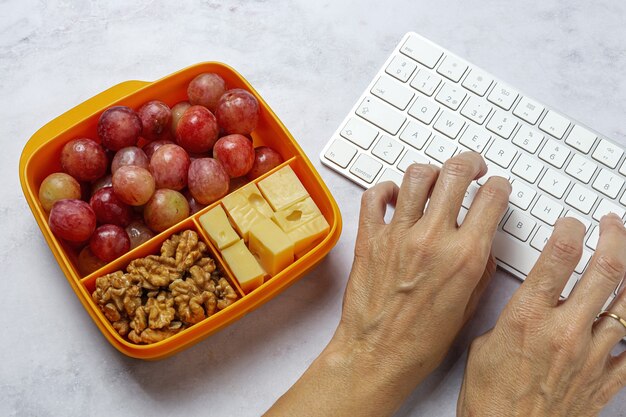 Alimentos saludables en envases de plástico listos para comer con queso, uvas y nueces en la mesa de trabajo. Para llevar nueces