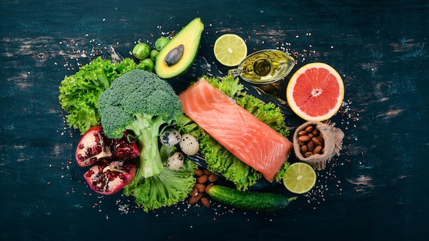 Alimentos saludables Pescado salmón aguacate brócoli verduras frescas nueces y frutas Sobre un fondo negro Vista superior Espacio de copia