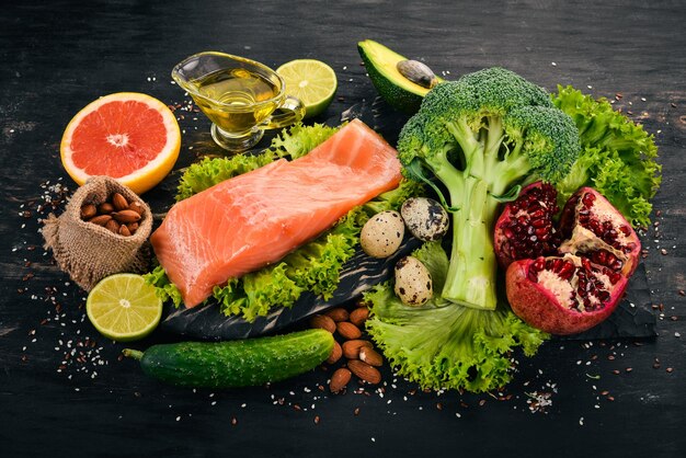 Alimentos saludables Pescado salmón aguacate brócoli verduras frescas nueces y frutas Sobre un fondo negro Vista superior Espacio de copia