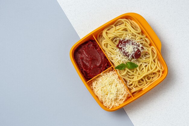 Alimentos saudáveis em recipientes plásticos prontos para comer com espaguete caseiro com tomate, queijo e manjericão na mesa de trabalho. Comida italiana. Para tirar.