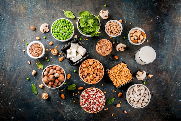 Alimentos veganos de dieta saudável, fontes de proteínas vegetarianas: Tofu, leite vegano, feijão, lentilha, nozes, leite de soja, espinafre e sementes. Vista superior na mesa branca.