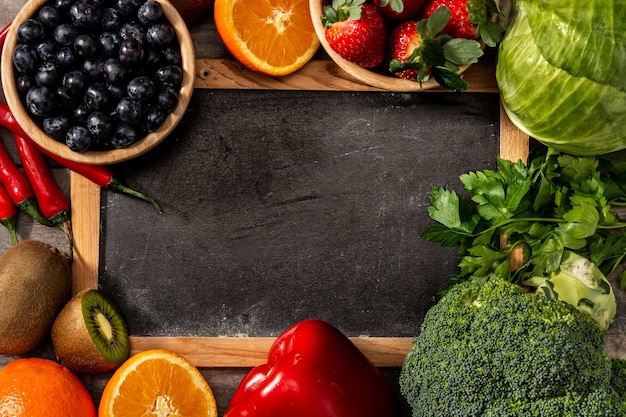 Alimentos vegetales saludables y pizarra en mesa de madera.