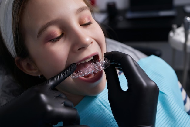 Alineador invisible de niña caucásica y apuntando a sus dientes rectos perfectos. Concepto de confianza y salud dental.