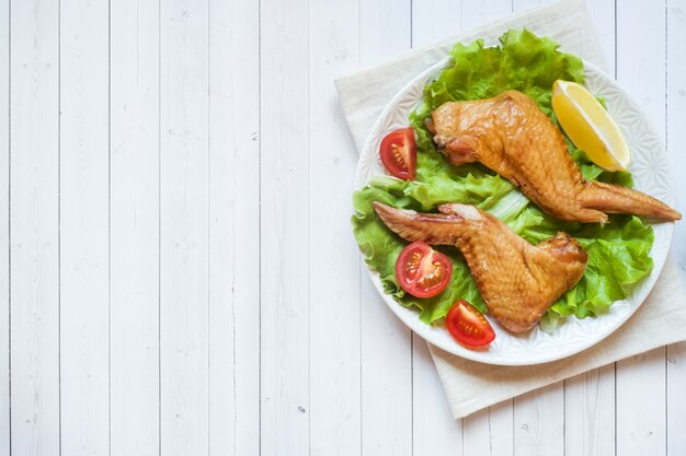 Alitas de pollo ahumadas con lechuga fresca tomate y limón. Copia espacio