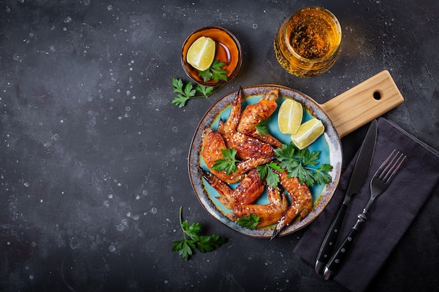 Alitas de pollo al horno con semillas de sésamo, perejil y lima en un plato y un vaso de cerveza