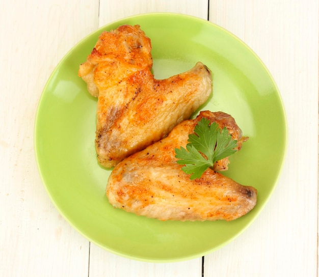 Alitas de pollo asadas con perejil en el plato sobre fondo blanco de madera primer plano