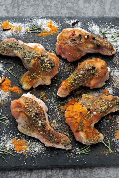 Alitas de pollo crudas marinadas en especias en un tablero de piedra negra.