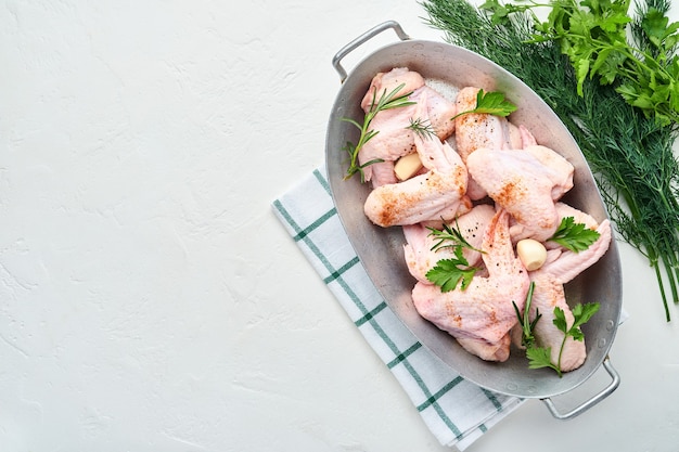 Alitas de pollo crudas en un recipiente blanco con especias e ingredientes para cocinar sobre una superficie de hormigón ligero