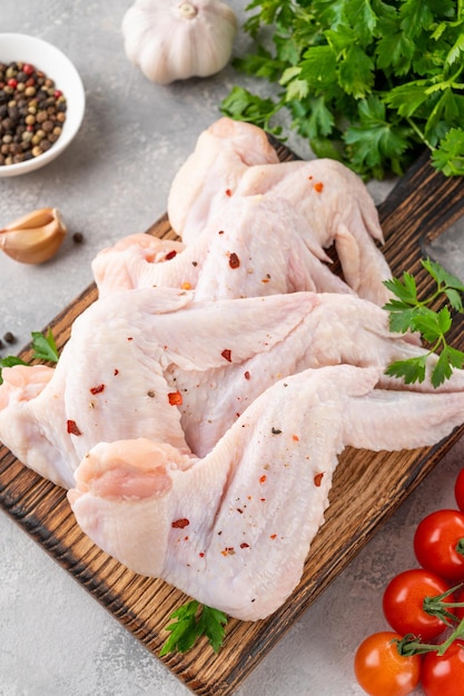 Alitas de pollo crudas en una tabla de cortar de madera con especias hierbas frescas tomates Cerrar