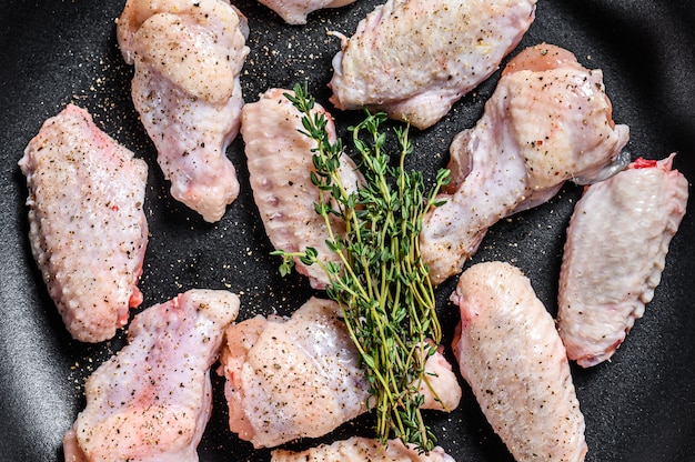 Alitas de pollo con especias y hierbas listas para cocinar en una sartén. Fondo gris