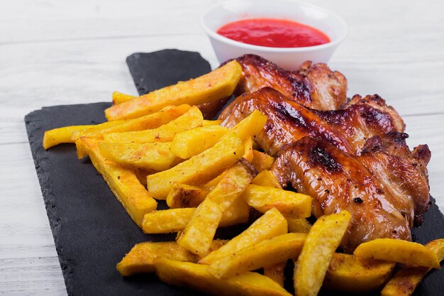 Alitas de pollo fritas y papas fritas en un plato negro con salsa de fondo de madera