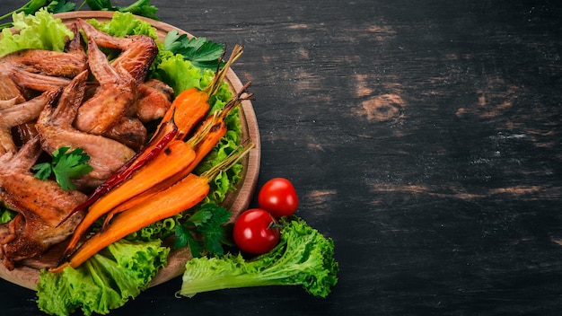 Alitas de pollo a la parrilla con verduras y zanahorias sobre un fondo de madera Vista superior Espacio de copia