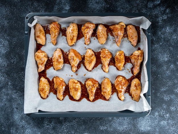 Alitas de pollo pegajosas con salsa de soja y miel sin cocer sobre una bandeja para hornear antes de cocinarlas en el horno