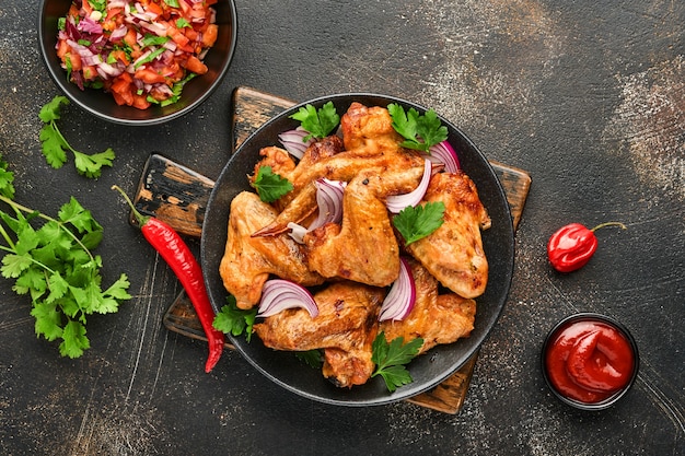 Alitas de pollo a la plancha o barbacoa asada con especias y salsa de tomate en un plato negro. Vista superior con espacio de copia.