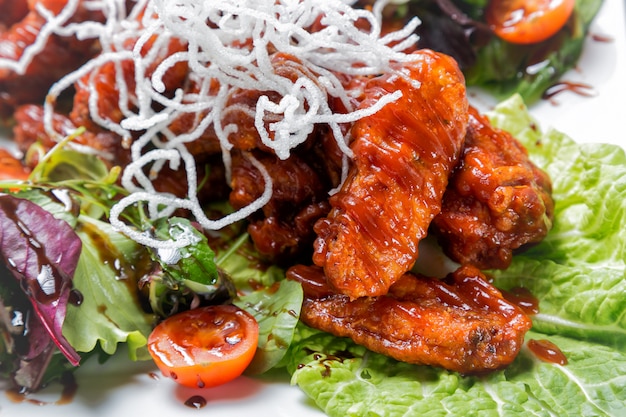 Alitas de pollo con salsa de barbacoa, ensalada, tomates y patatas fritas en un plato blanco