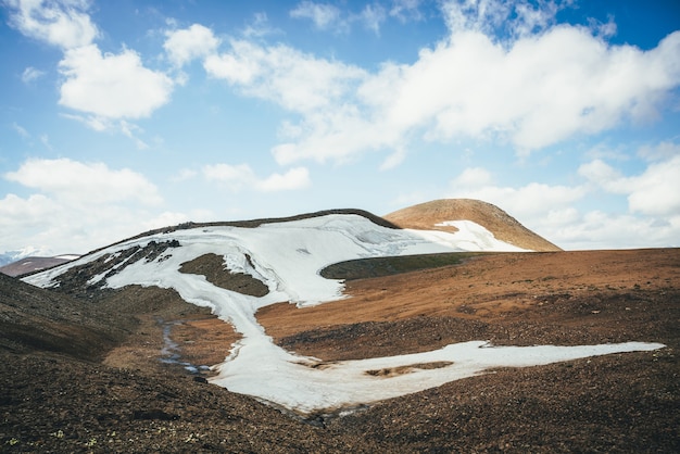 Alivio del desierto de montaña soleada con glaciar en la luz del sol bajo un cielo nublado azul. Pintoresco paisaje de las tierras altas con un pequeño glaciar en lo alto de las montañas en las colinas. Paisaje de montaña minimalista del desierto de las tierras altas.