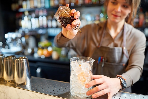 Alkoholgetränke, Menschen und Luxuskonzept - Barkeeperin mit einem Glas Eis und Sirup bereitet Cocktails an der Bar zu