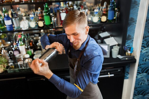 Alkoholgetränke, Menschen und Luxuskonzept - glücklich lächelnder Barmann mit Shaker, der an der Bar einen Cocktail zubereitet