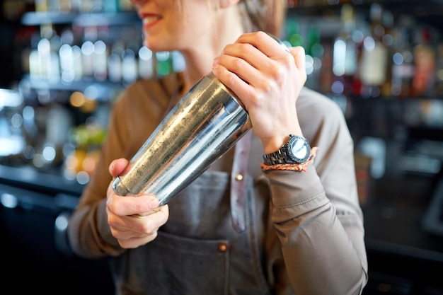 Alkoholgetränke, Menschen und Luxuskonzept - Nahaufnahme einer lächelnden Barkeeperin mit Stahlshaker, die an der Bar einen Cocktail zubereitet