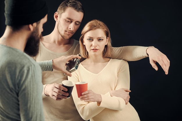 Alkoholische Freundschaft Männer Frau auf nachdenklichen Gesichtern schwarzem Hintergrund Männer gießen Womans Tasse mit Alkohol