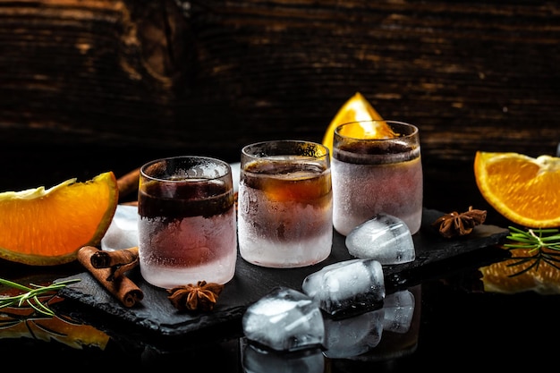 Alkoholische Getränke aus gefrorenem Schnapsglas auf rustikalem Holzhintergrund Schnapsglas Kräuterlikör mit Zimt und Orangen auf dunklem Hintergrund Catering-Banner-Menü Rezept Ort für Text