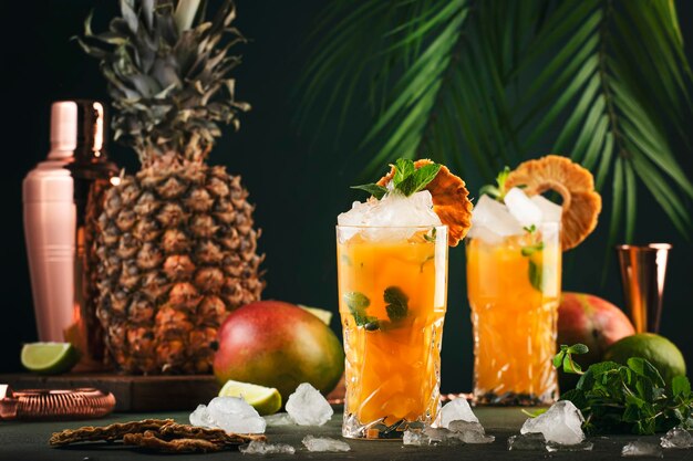 Alkoholischer Cocktail mit Wodka-Ananassaft Mango-Likör-Eis Longdrink oder Sommermocktail Tropischer dunkler Hintergrund mit Palmblättern und exotischen Früchten