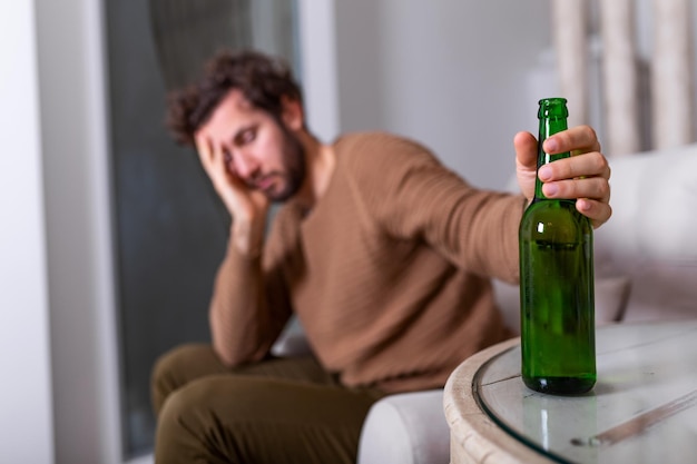 Alkoholischer Mann, der nach einer Flasche Bier greift, Mann, der allein zu Hause trinkt. Alkoholismus, Alkoholsucht und Menschenkonzept - männlicher Alkoholiker mit einer Flasche Bier, die allein zu Hause trinkt